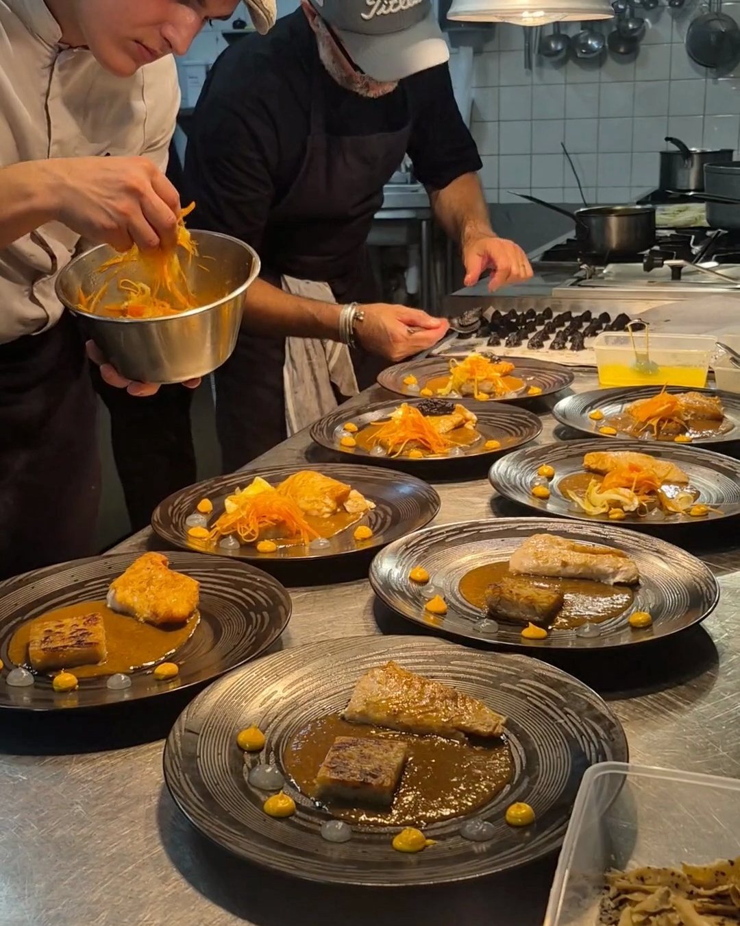Two chefs from the Brigade plating a series of dishes